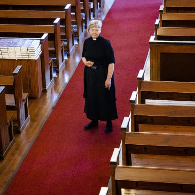 Nainen kirkon keskikäytävällä papin vaatteissa.