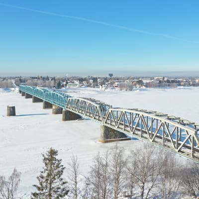Haaparannan ja Tornio välinen rautatiesilta kulkee Tornionjoen yli. Kuva on otettu talvella ja joki on jäässä. Taistalla häämöttää Haaparanta.
