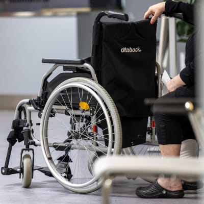 En person sitter i aulan och har sin hand på en rullstol. 