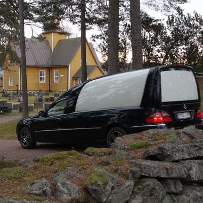 En svart begravningsbil kör in på kyrkogården i Dragsfjärd