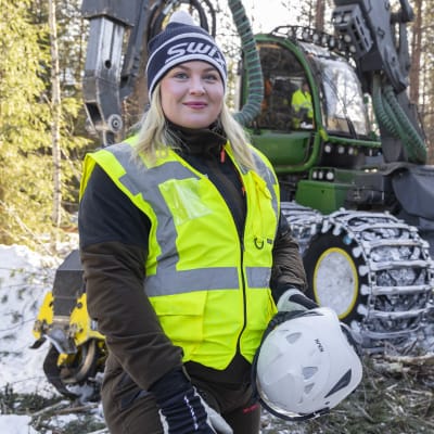 Metsä Groupin metsäasiantuntija Anni Väisänen poseraa hakkuukoneen edessä.