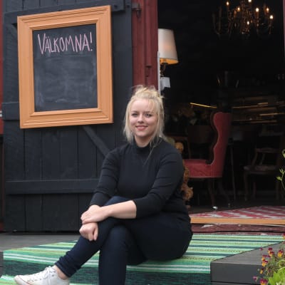 Ellen Järvinen sitter på trappan framför en öppen dörr till till sitt café Källarvinden i Kasnäs