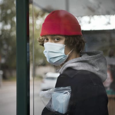 En kille som bär munskydd står invid en busshållplats.