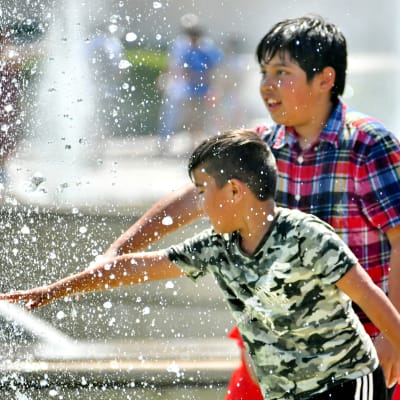 Två pojkar som sträcker ut händerna så de når vattenstrålarna som sprutar ut från en fontän.