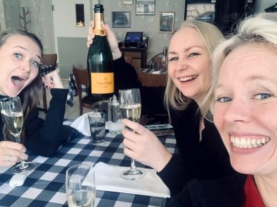 Tre glada kvinnor sitter vid ett bord och skålar i champagne.