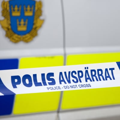 Närbild på platsband där det står "polis avspärrat" framför en svensk polisbil.