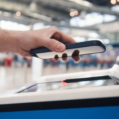 En person håller i en smarttelefon med skärmen neråt mot en läsare på en flygplats.