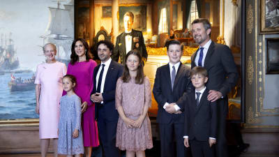 Familj poserar framför ett stort porträtt