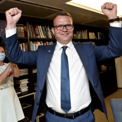 Petteri Orpo, en man i kostym och glasögon pumpar sina händer i luften.