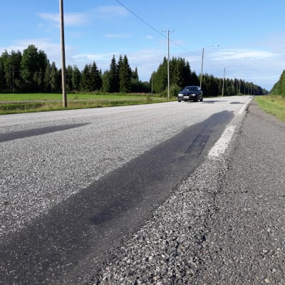 Henkilöauto ajaa kesäisellä paikatulla maantiellä.