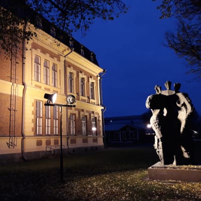 Valonheittimet valaisevat Joensuun taidemuseon päätyä ja Maiju Lassilan patsasta syksyn yössä.  
