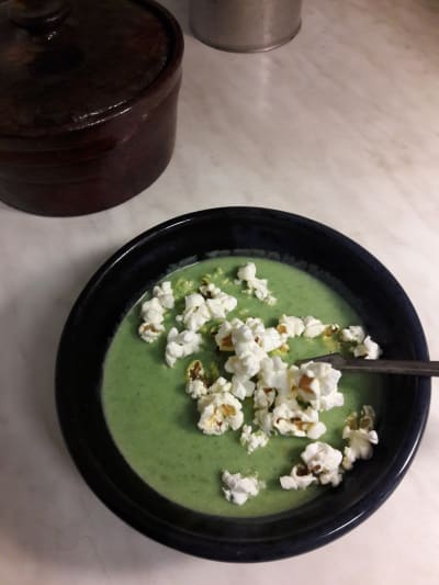 Grön soppa med popcorn i en svart talrik.