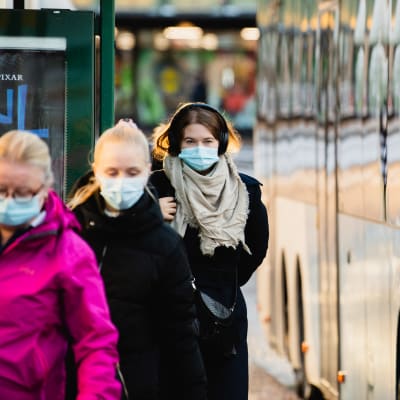 Ihmisiä hengityssuojaimet kasvoilla bussipysäkillä Sörnäisissä.
