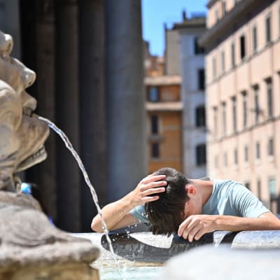 Ett barn fuktar sitt huvud med vatten vid en fontän.