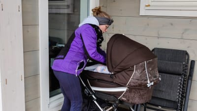 En kvinna i lila jacka sköter om en baby som ligger i en barnvagn.