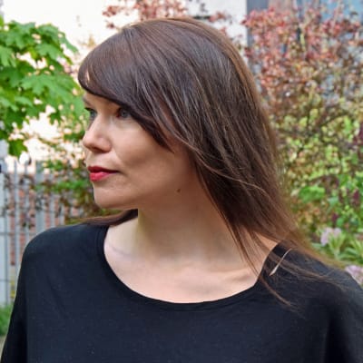 Författaren Hannele Mikaela Taivassalo poserar i Morgonöppets trädgård.