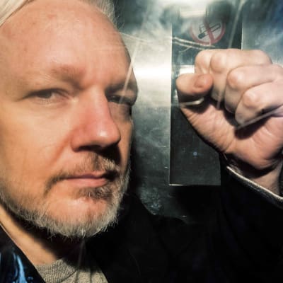 Julian Assange gestikulerar till pressfotografer under en fångtransport till en domstol i London den första maj 2019.