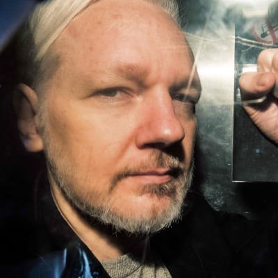 Julian Assange gestikulerar till pressfotografer under en fångtransport till en domstol i London den första maj 2019.