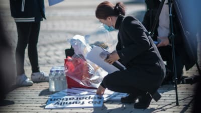 En kvinna med munskydd på knä på gatan ställer demonstrationsplakat i ordning.