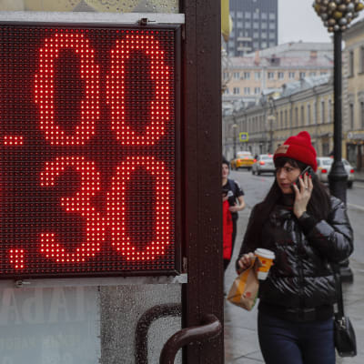 En kvinna passerar en skylt med rubelns valutakurs.
