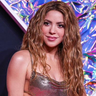 Närbild av Shakira som poserar på en röd matta. Hon tittar åt sidan och ler. Hon är klädd i en guldig klänning och har håret utsläppt.