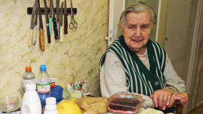 En äldre dam sitter vid sitt köksbord och tittar på de livsmedel hon har fått ta emot