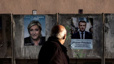 Äldre man tittar på valplakat för Marine Le Pen och Emmanuel Macron.