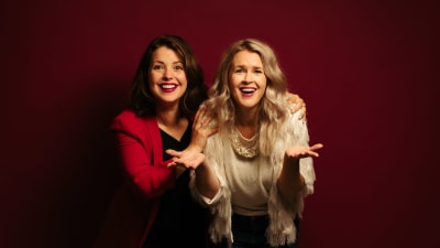 Två leende kvinnor framför röd vägg