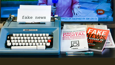 ett skrivbord med en skrivmaskin med ett papper där det står fake news och böcker som handlar om att identifiera falska nyheter