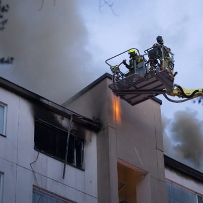Två brandmän i lyftkran släcker en eldsvåda i ett höghus i Lahtis.