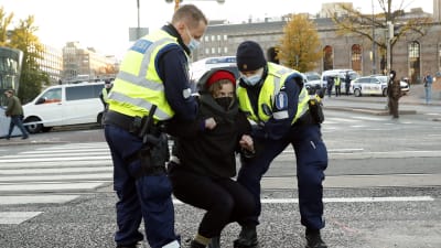 Två poliser lyfter upp en kvinna från marken under en Elokapina-demonstration.