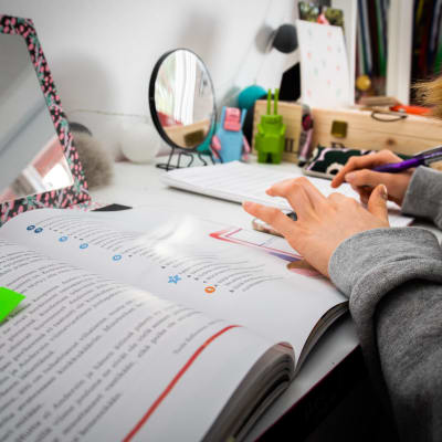 En ung flicka studerar på distans. Hon har framför sig en bok på ett skrivbord.