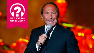 Paul Anka ler och sjunger i en mikrofon som han håller i handen.