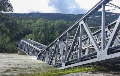 Närbild av stora gråa broelement som delvis ligger i vattnet i en älv.