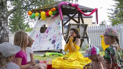 Ammattiprinsessa istuu lasten ympärillä syntymäpäiväjuhlilla.