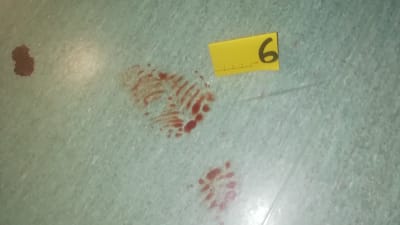 Ett blodigt fotspår från en sko med randigt mönster. Bredvid skoavtrycket finns en gul brottsutredningslapp med siffran sex.