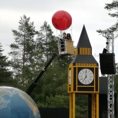 En röd ballong som lfter till väders med folk i korgen, pjäsen Jorden runt på 80 dagar på Raseborgs sommarteater.