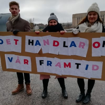 Tre unga demonstranter med ett plakat med texten "Det handlar om vår framtid".