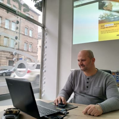 En man sitter framför en dator vid ett skyltfönster.