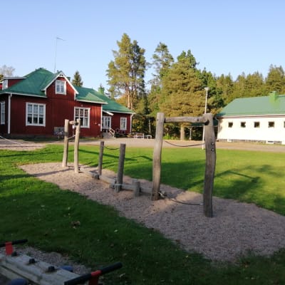 En röd träbyggnad och en ljust stenhus som är Västankvarns skola i Ingå.
