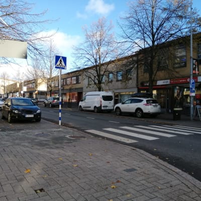 En gata som går genom Lojo centrum där det står bilar parkerade vid sidorna.