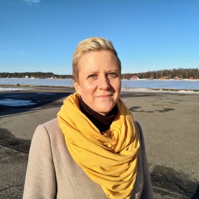 En kvinna med kort blont hår med en gul scarf runt halsen.