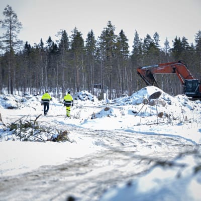 Tre män i arbetskläder går omkring på gruvdriftsområde. Snö ligger på marken och en grävmaskin syns i bakgrunden.