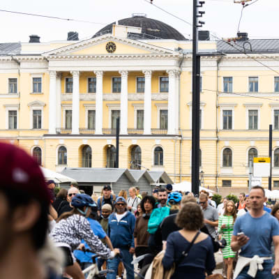 Människor på Senatstorget i Helsingfors. Regeringsbyggnaden i bakgrunden. 