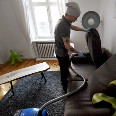 Städaren  Bayron Boloyi dammsuger soffan ett privat hem i Helsingfors i mars 2018. 