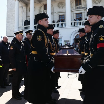 Soldater i uniform bär på en kista. Bredvid står soldater som håller en stor sorgkrans.