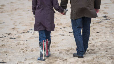 Man och kvinna går på stranden, håller varandra i handen