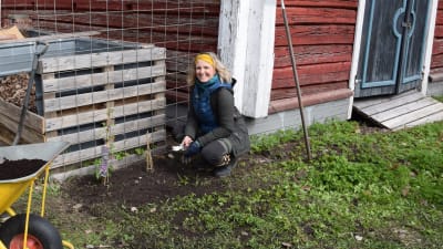 Leende kvinna sitter på huk bredvid en plantering