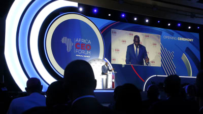 En man, Makhtar Diop, står vid ett podium och syns också på en stor duk intill. Bredvid honom finns logotypen för Africa CEO Forum. I förgrunden syns silhuetter av huvuden på personer i publiken.