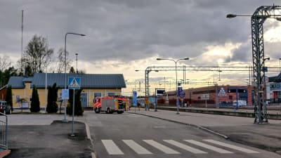 En brandbil står parkerad utanför en gul träbyggnad som är en järnvägsstation. Till höger löper järnvägsspåren.